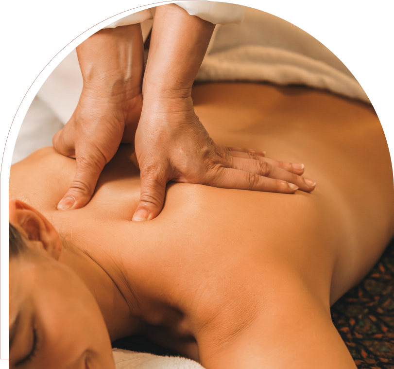 Person receiving a back massage, lying face down on a towel, with hands applying pressure on the upper back.